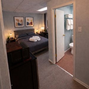 Inside one of the queen bed rooms with view of bathoom, fridge & microwave and bed