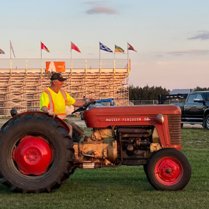 Man driving a tractor in the field with the exhibition stands in the background during a sunset