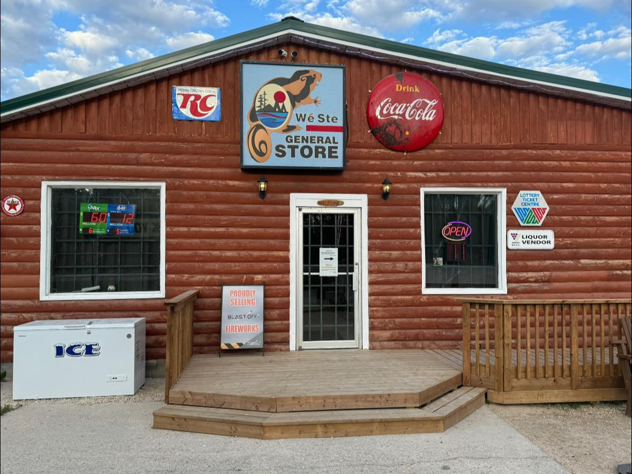 Wood siding Wanless General store with the vintage Wé Ste General Store sign, CocaCola and Royal Crown Cola RC signs. They have a small deck in front and other signs surrounding the two large windows. 