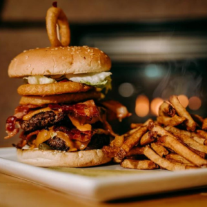 plate piled high with double patty and onion ring burger nad homemade fries