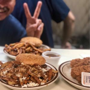 plates of burgers with poutine and chicken fingers with a blur image of boy holding hands in peace sign.