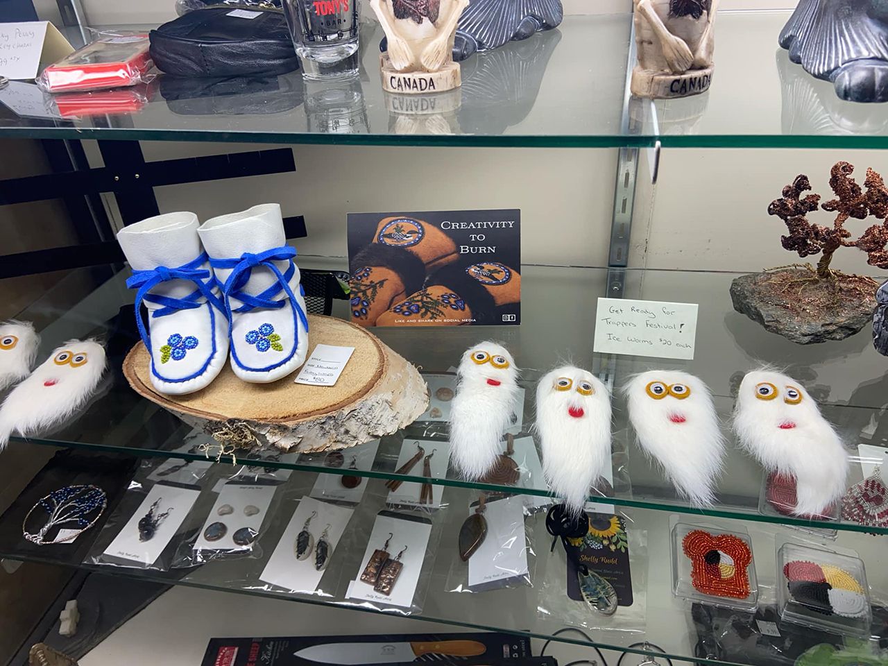 Glass display case, showcasing gifts made by Shauna. Including Trappers' ice worms, infant white & blue beaded wraparounds, earrings and other giftware