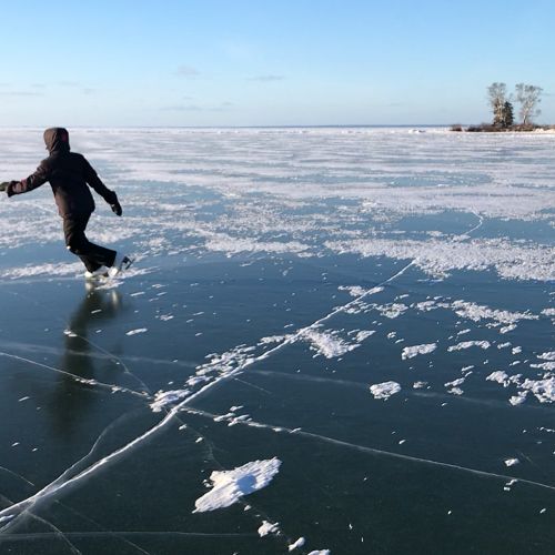 Woman skating on clear, dark, deep lake ice